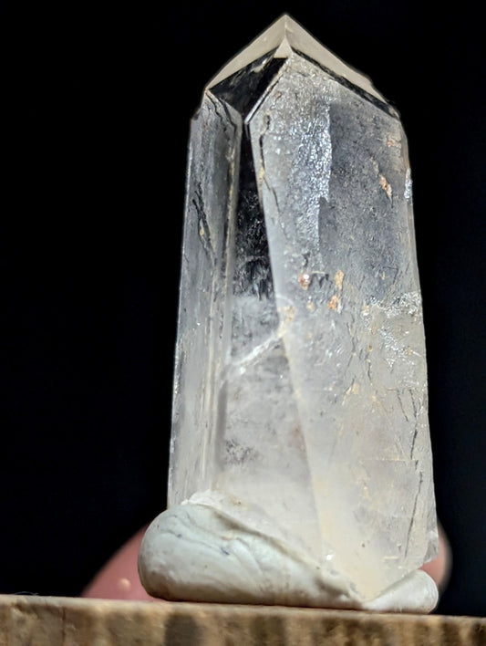 A translucent, clear quartz crystal with a pointed top and natural inclusions.