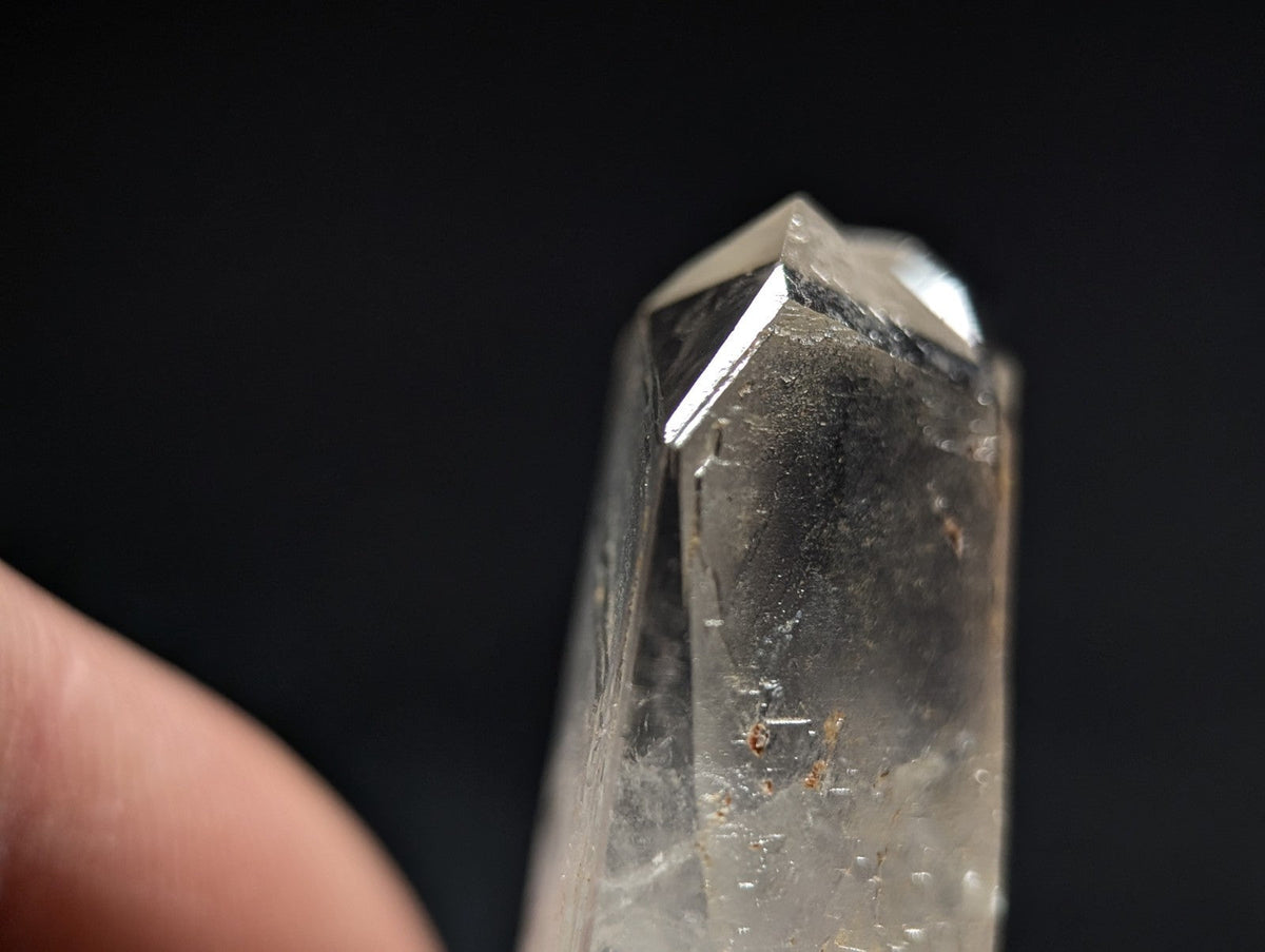 A clear quartz crystal with a pointed tip and visible internal inclusions, held against a dark background.