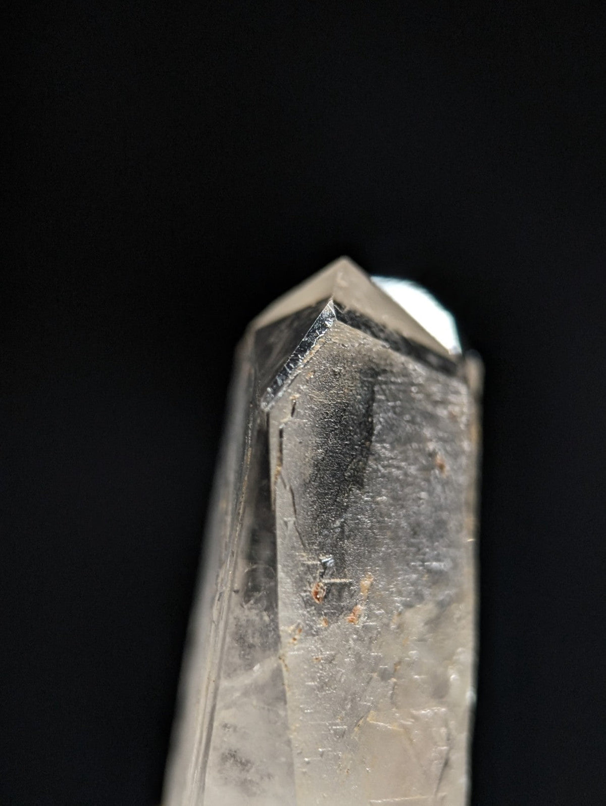 A clear quartz crystal with a pointed tip and visible internal inclusions, featuring natural translucency and subtle gray veining.