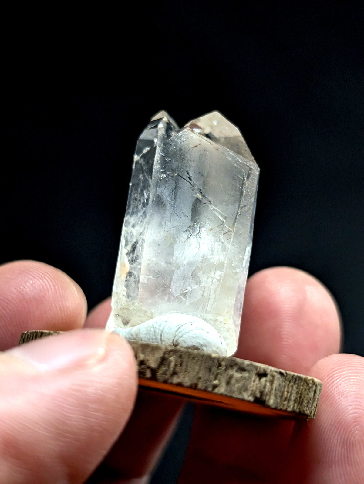 A translucent, clear quartz crystal with natural internal inclusions and a pointed top, held upright on a rustic wooden base.