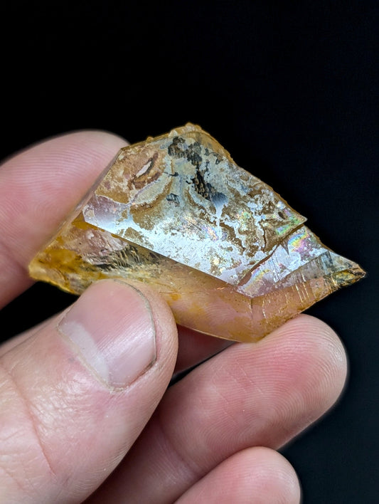 A translucent amber-colored crystal with iridescent, metallic streaks and a faceted surface.