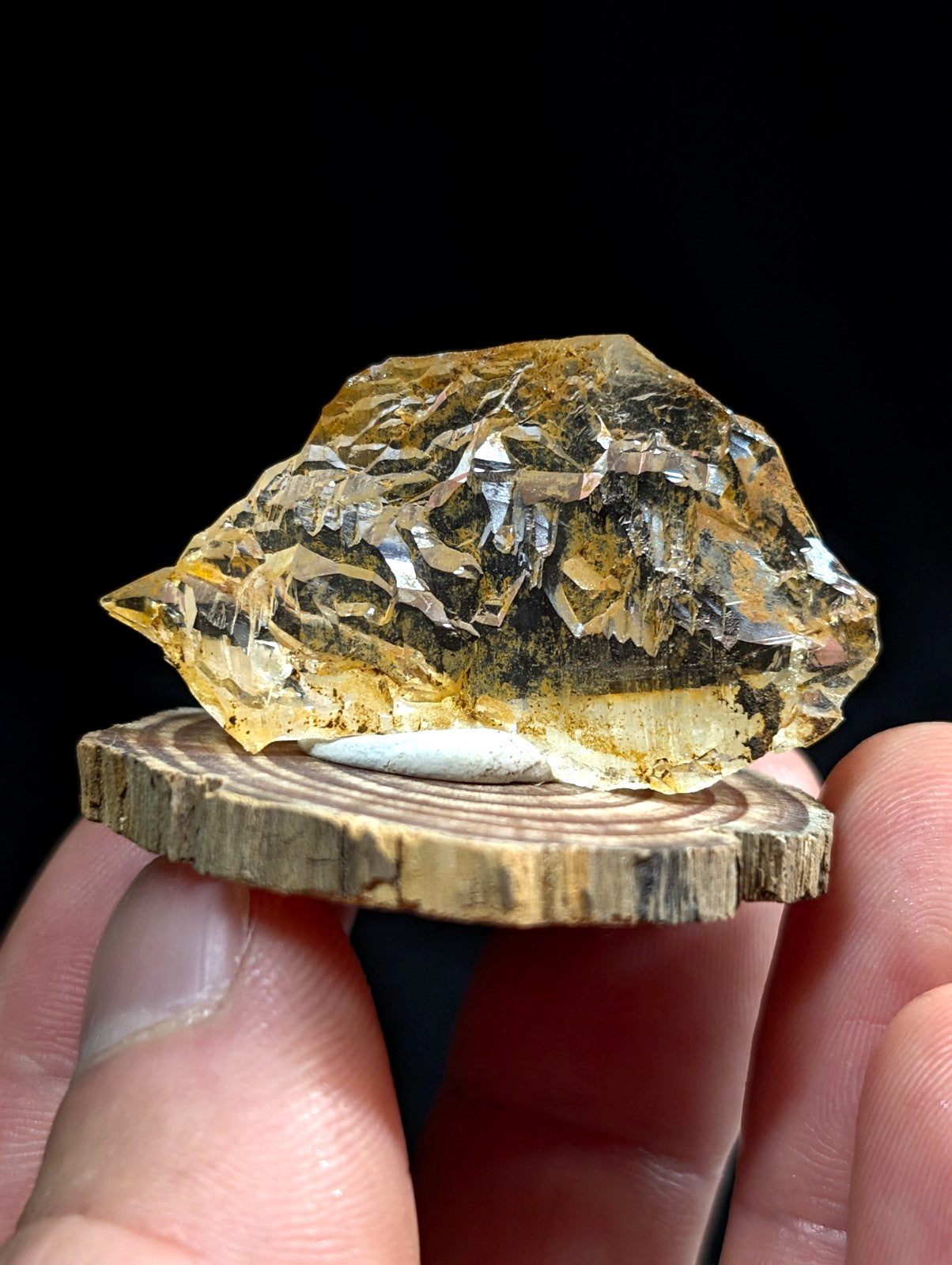 A unique etched quartz crystal point in translucent golden yellow with sharp jagged edges on a rustic wooden base