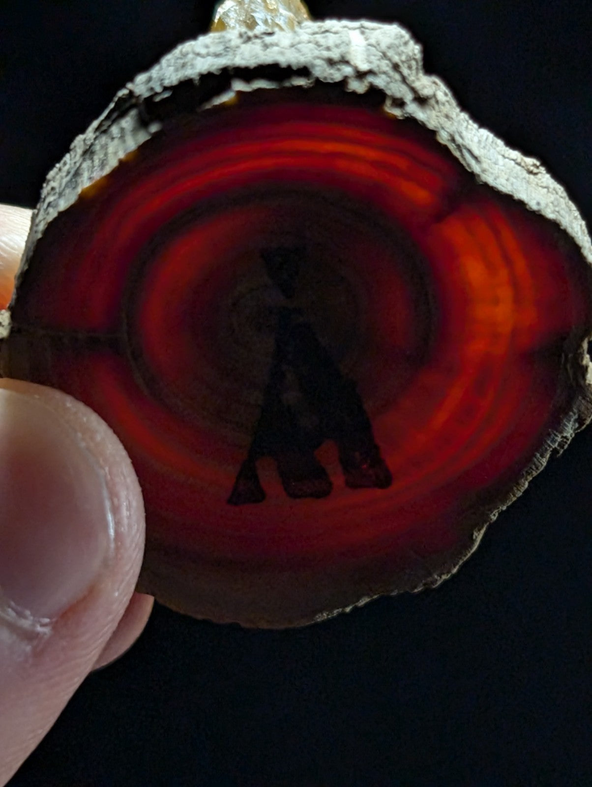A circular, translucent red agate slice with concentric bands and a dark silhouette of an hourglass engraved at its center.