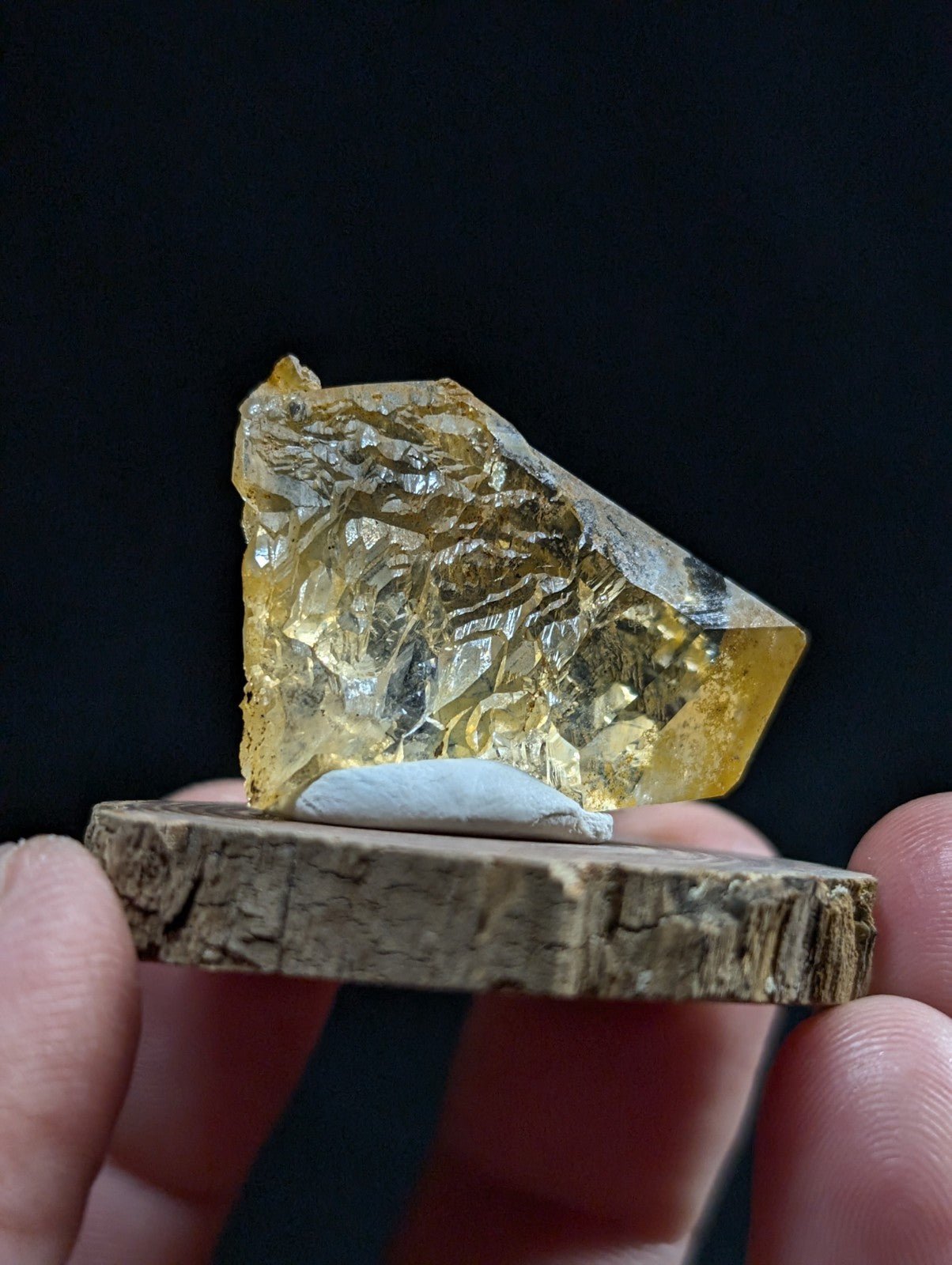 A translucent golden-yellow crystal with a rough, faceted surface rests on a rustic wooden base.