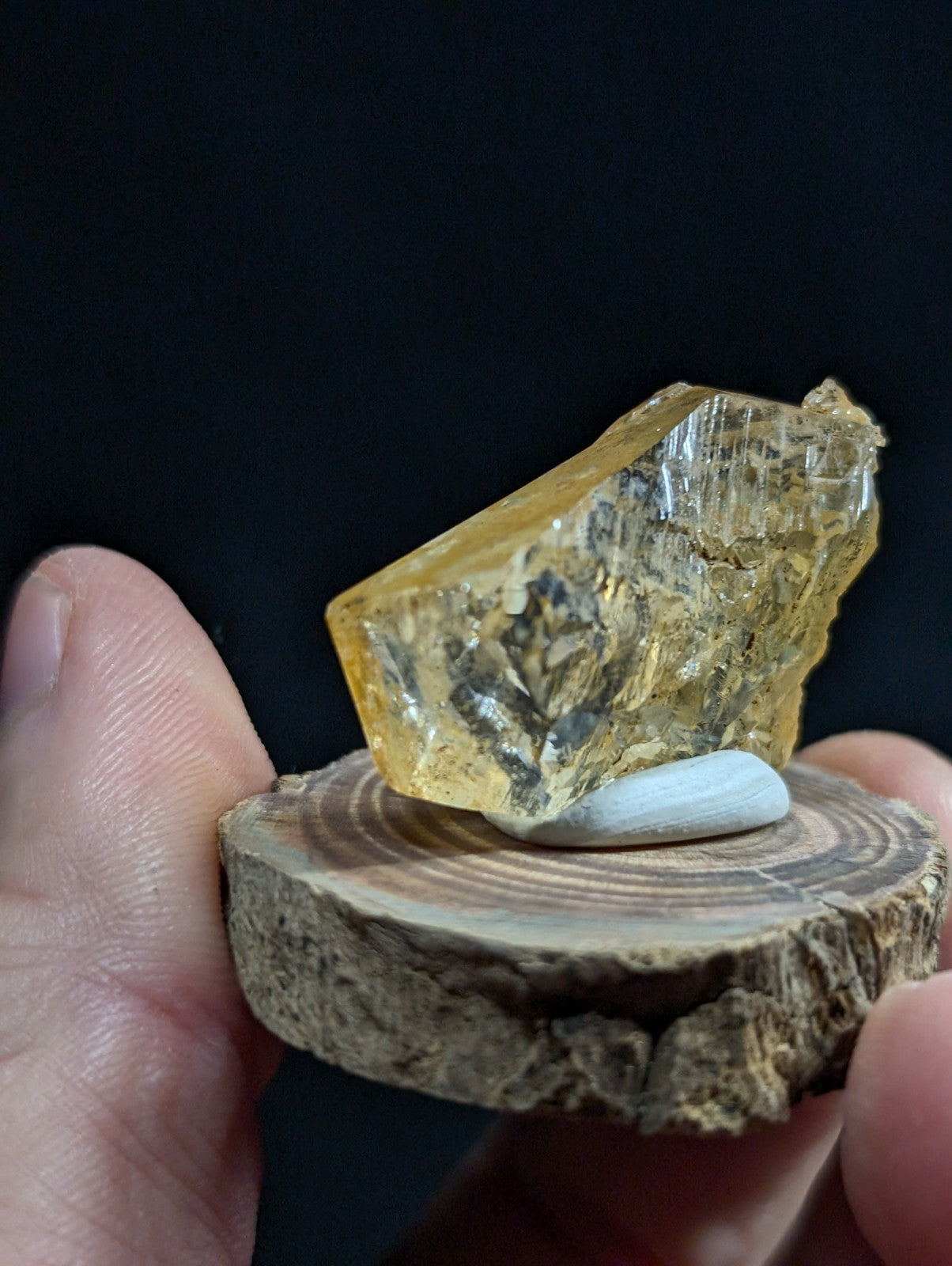 A translucent golden-yellow mineral specimen with crystalline facets and internal inclusions, displayed on a rustic wooden slice.