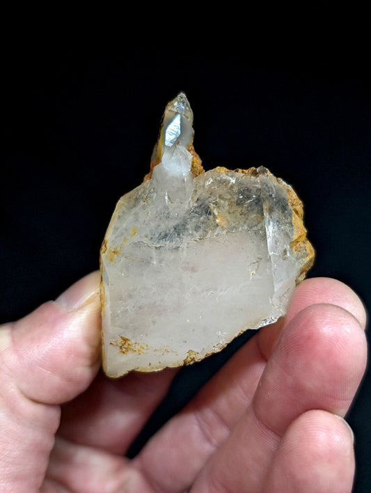 A translucent, pale quartz crystal with a pointed tip and earthy orange-brown matrix holding it together.