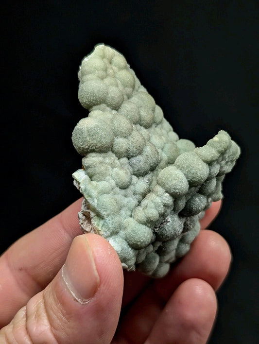 A pale green, textured mineral specimen with a bumpy, clustered surface held in hand.