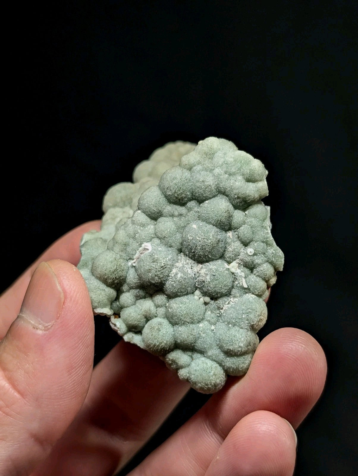 A pale green, bumpy mineral specimen with a textured surface held in hand.