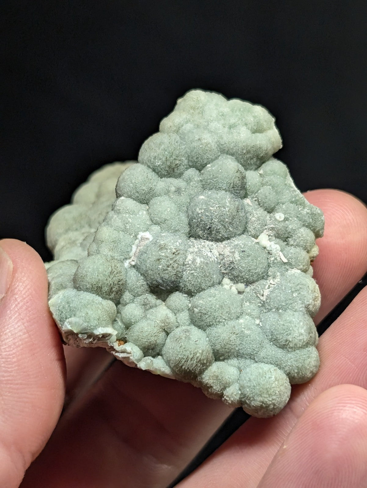 A pale green, bumpy mineral specimen with rounded nodules clustered together.