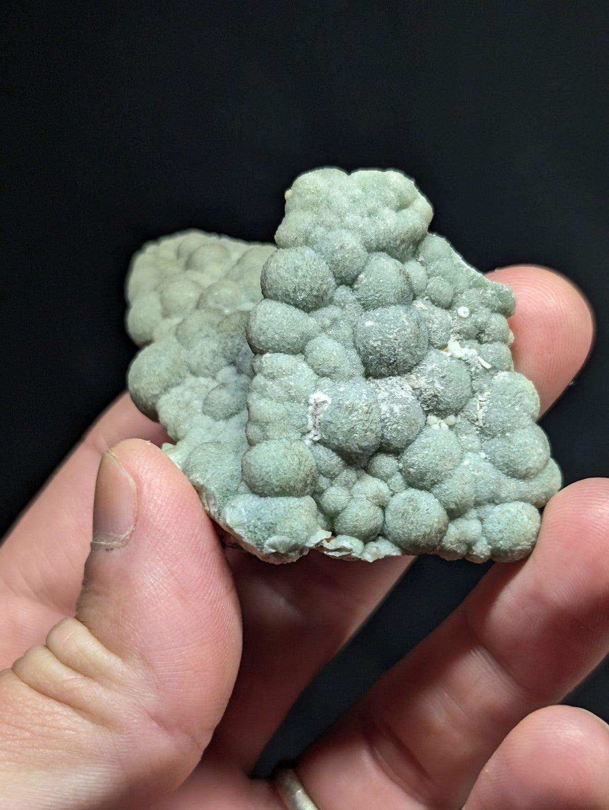A pale green, bubbly mineral specimen with a textured surface held in hand.