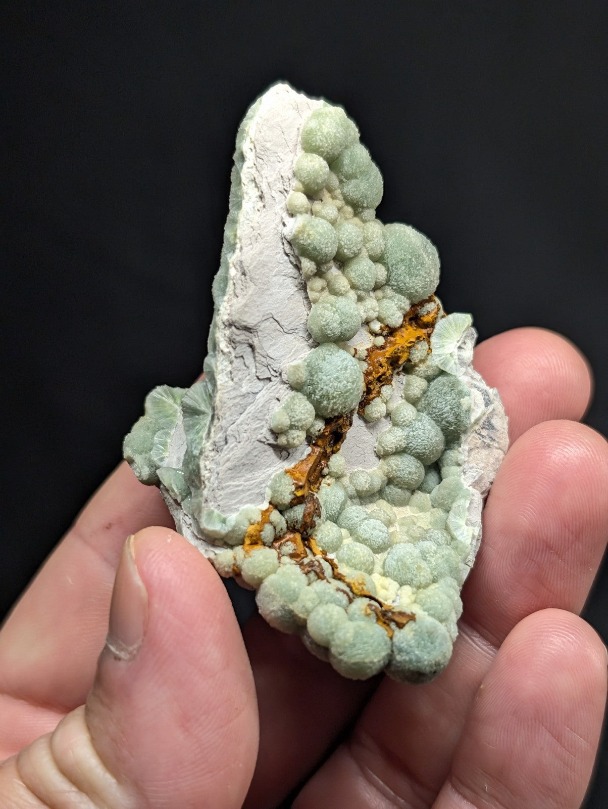 A hand holds a striking greenish-white mineral specimen featuring rounded, bubble-like formations clustered along its surface.