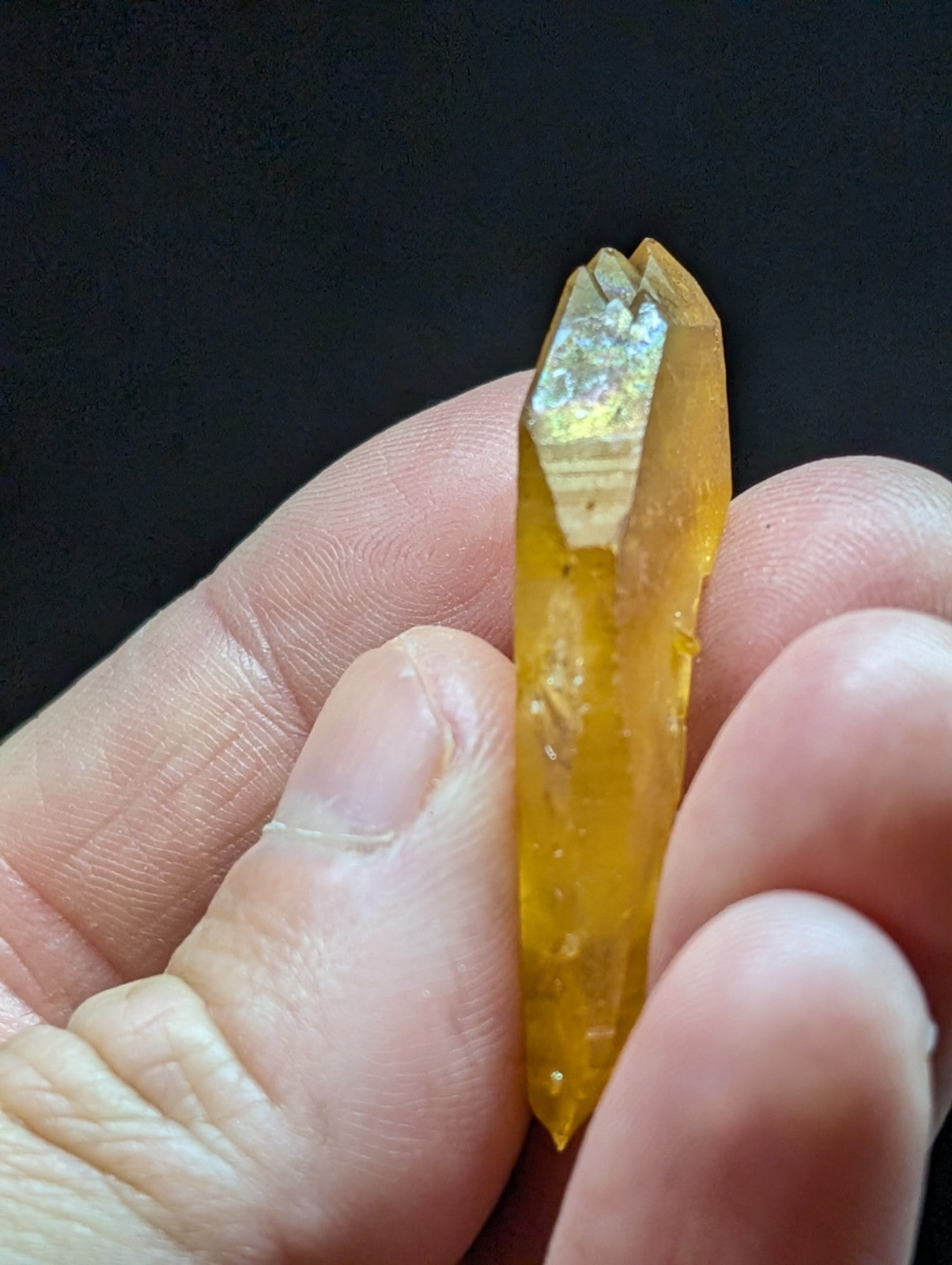 A translucent golden-yellow crystal with a pointed, faceted tip and natural striations.