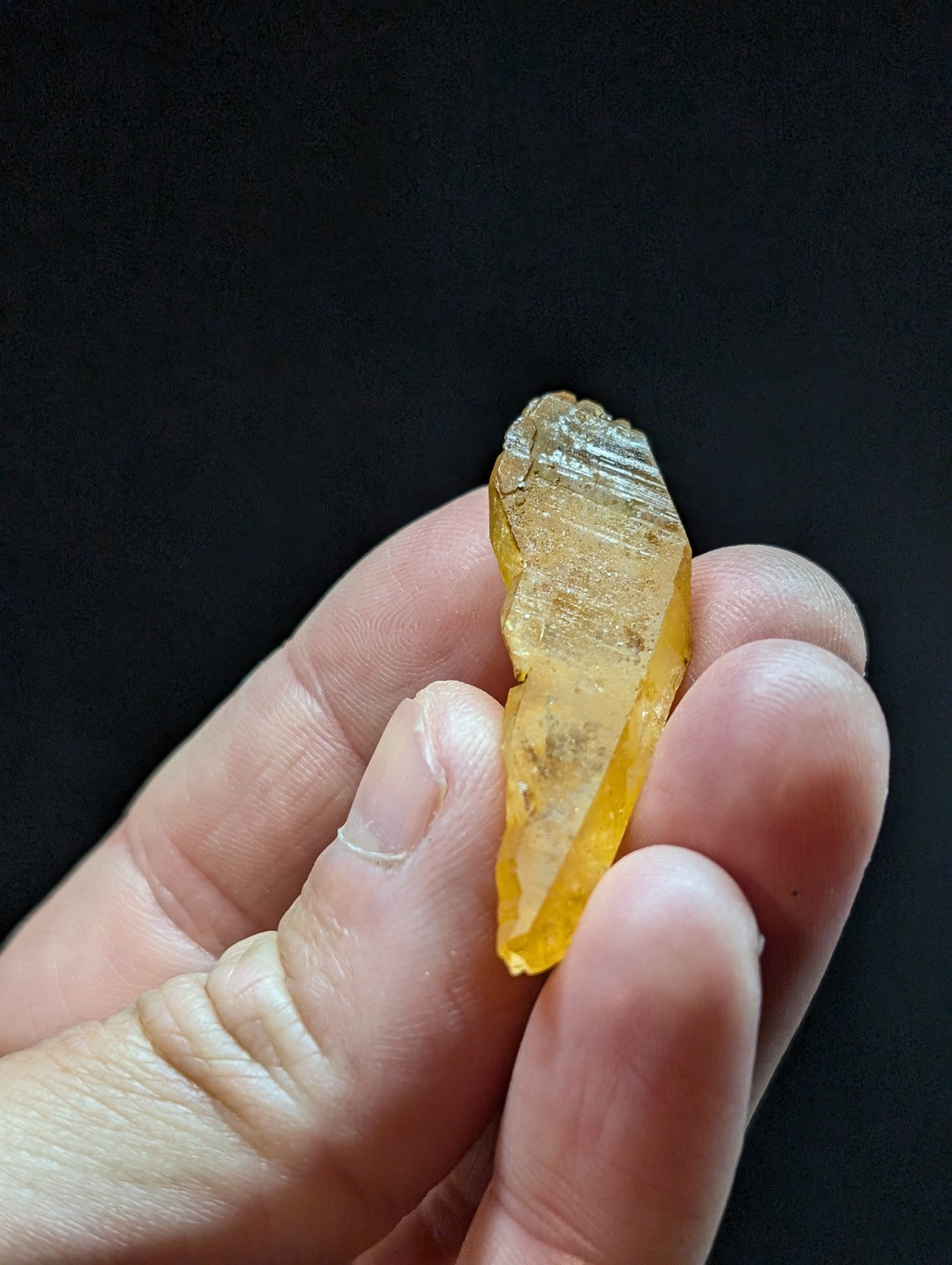 A translucent yellow crystal with a pointed tip and striated surface, held gently in someone’s hand.