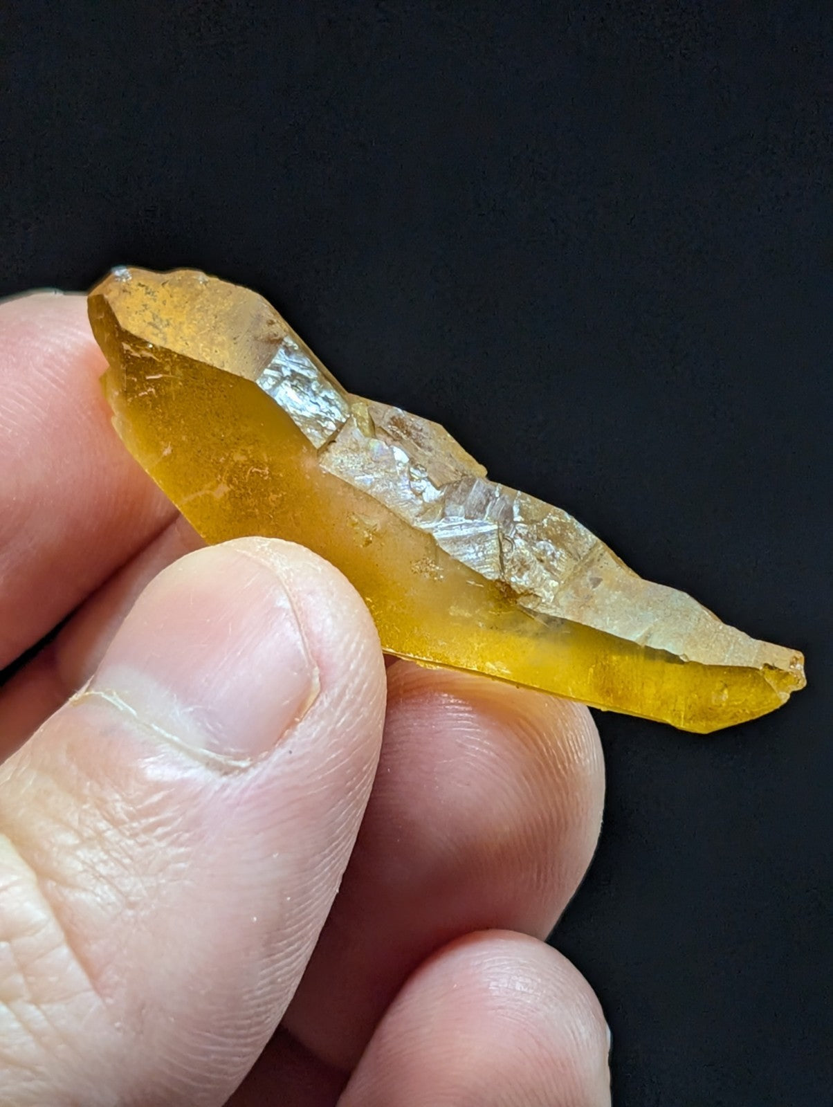 A translucent amber-colored crystal with a jagged, natural edge and internal reflective facets.