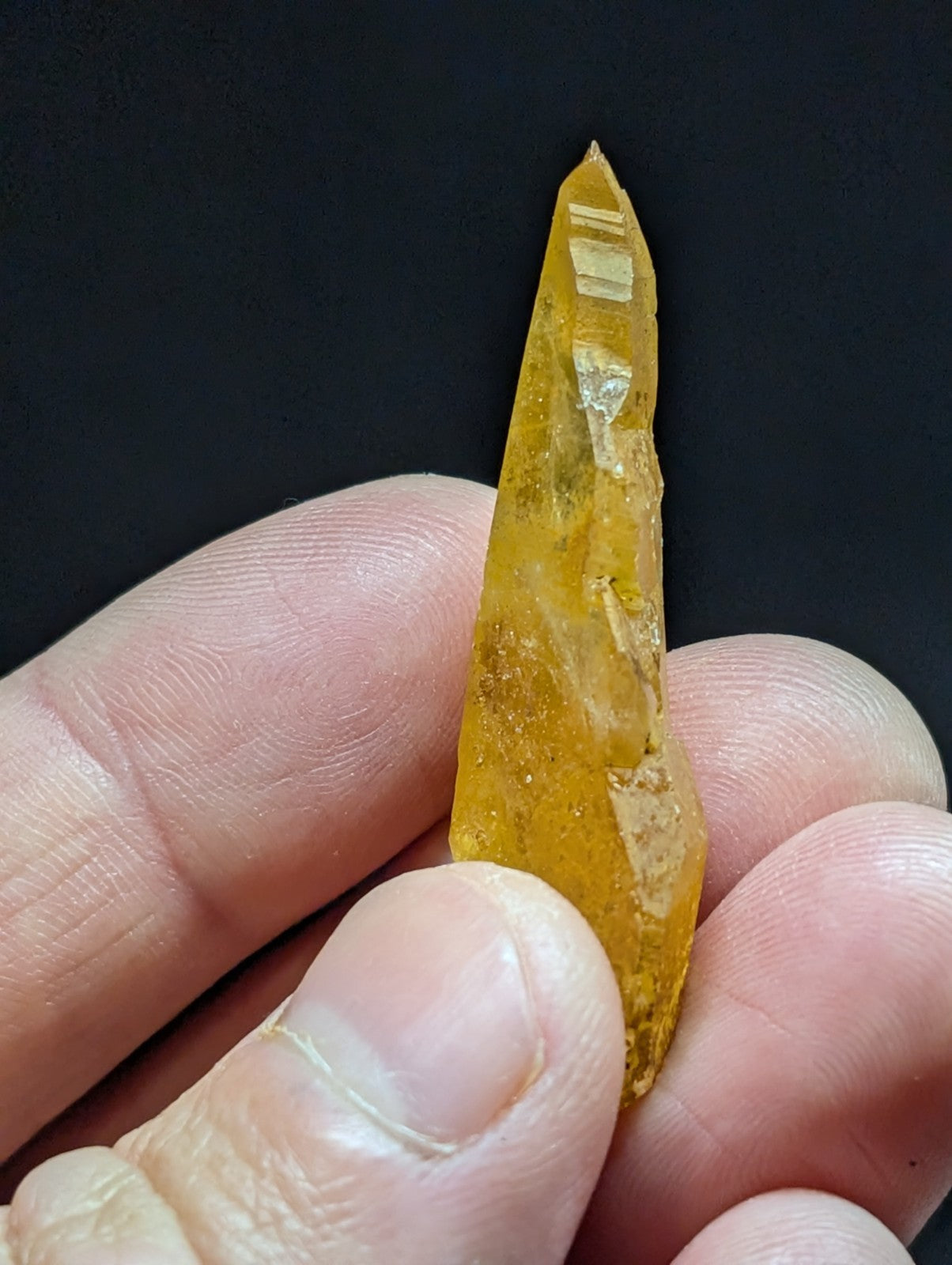 A translucent golden-yellow crystal with a pointed tip and visible internal striations, held gently between fingers.