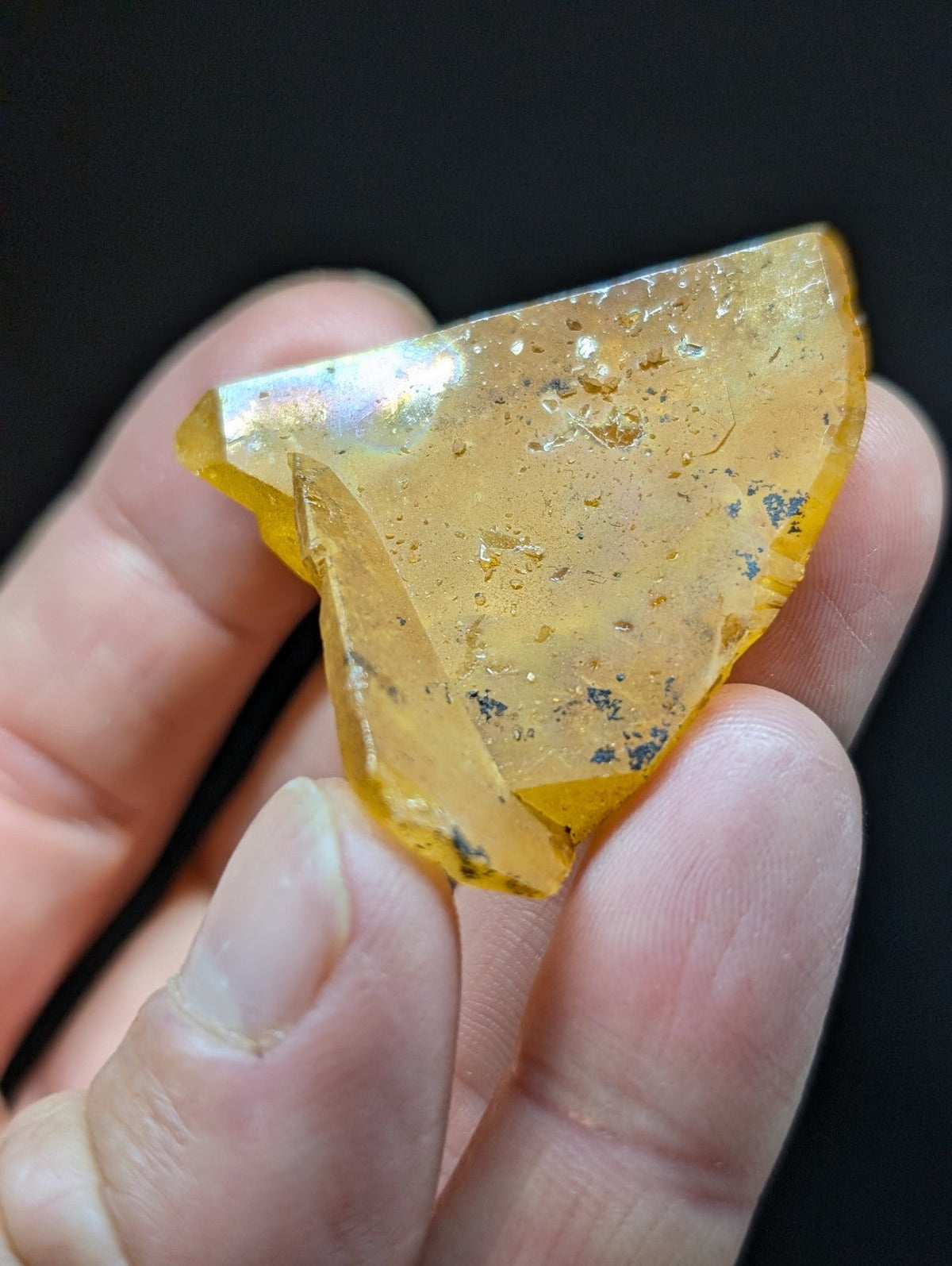 A translucent amber-colored fossilized resin fragment with a glossy, slightly iridescent surface and embedded dark inclusions.