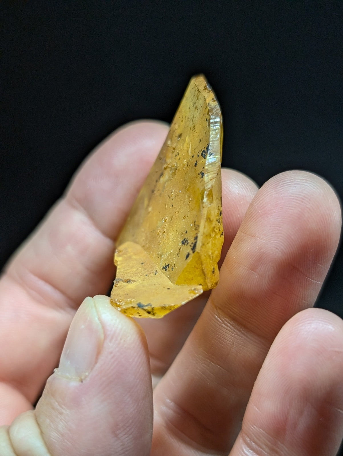 A translucent golden-yellow crystal with a pointed, faceted tip and subtle internal inclusions.