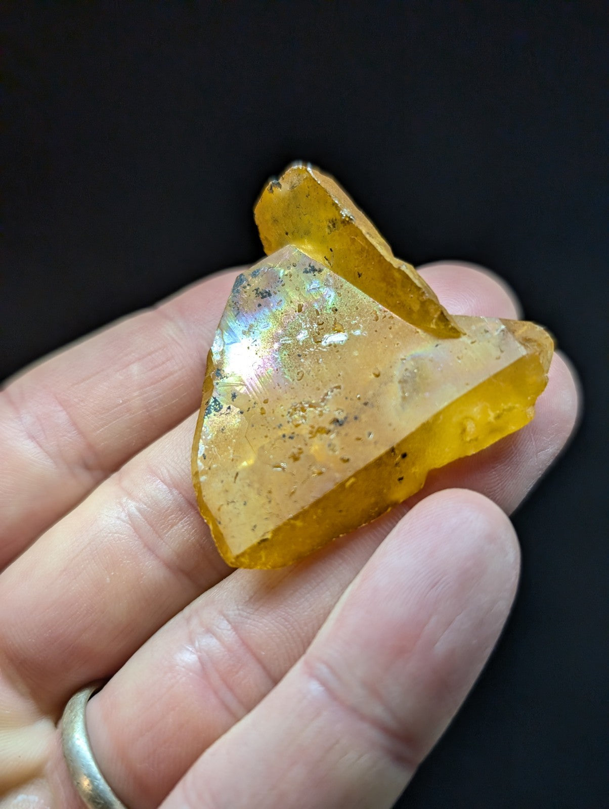 A translucent amber-colored fossilized resin fragment with a glossy, iridescent sheen and embedded dark specks.