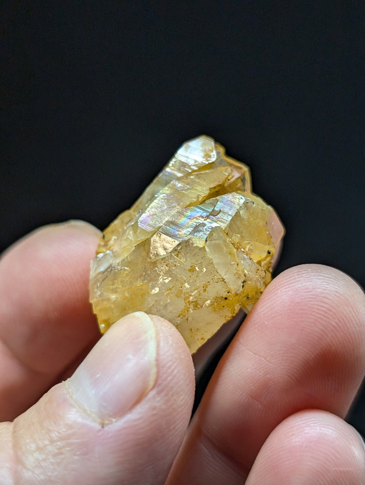 A translucent yellow crystal with iridescent facets, held gently between fingers.