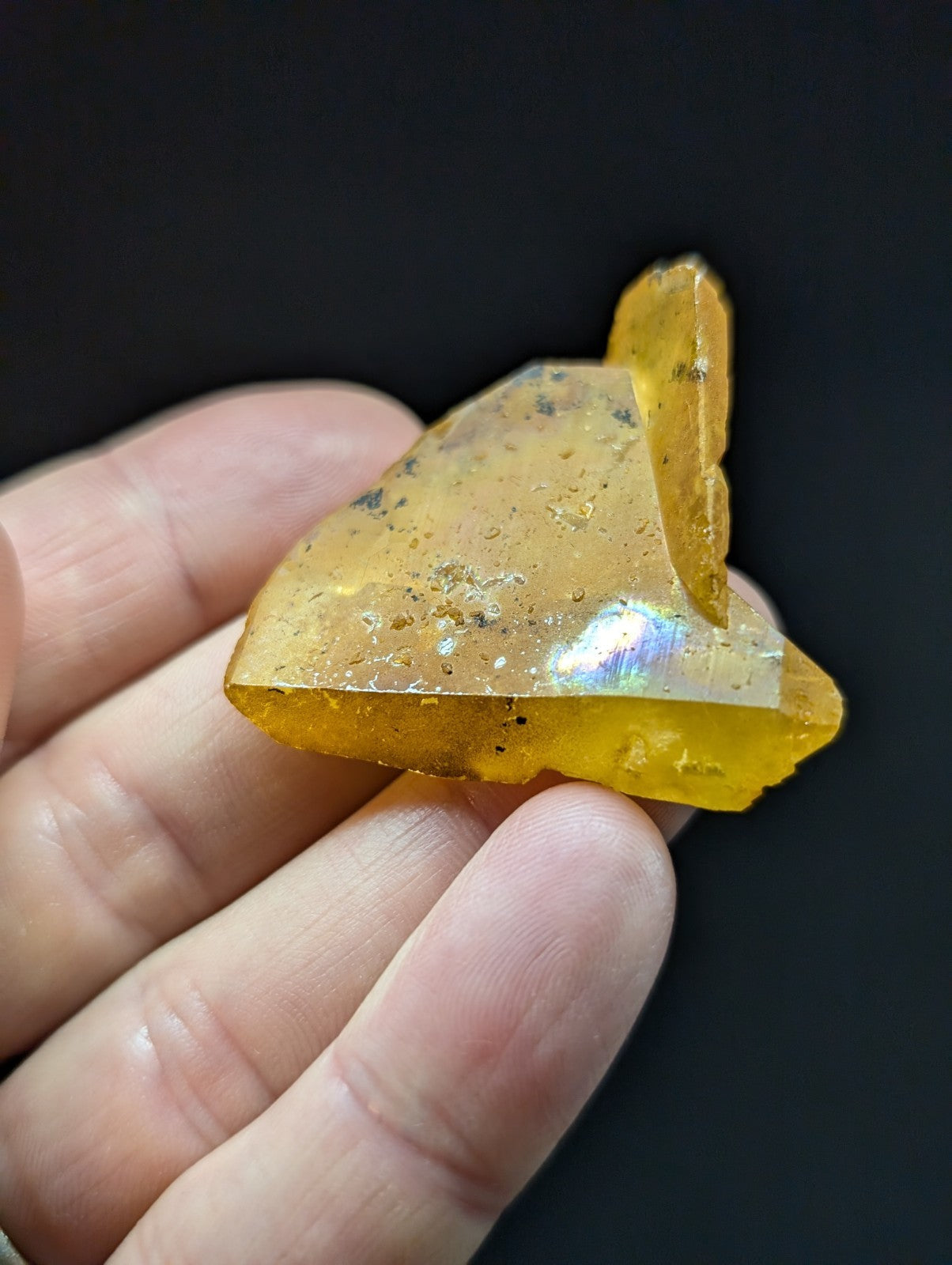 A translucent amber-colored, irregularly shaped piece of natural resin with embedded dark inclusions and a glossy surface.