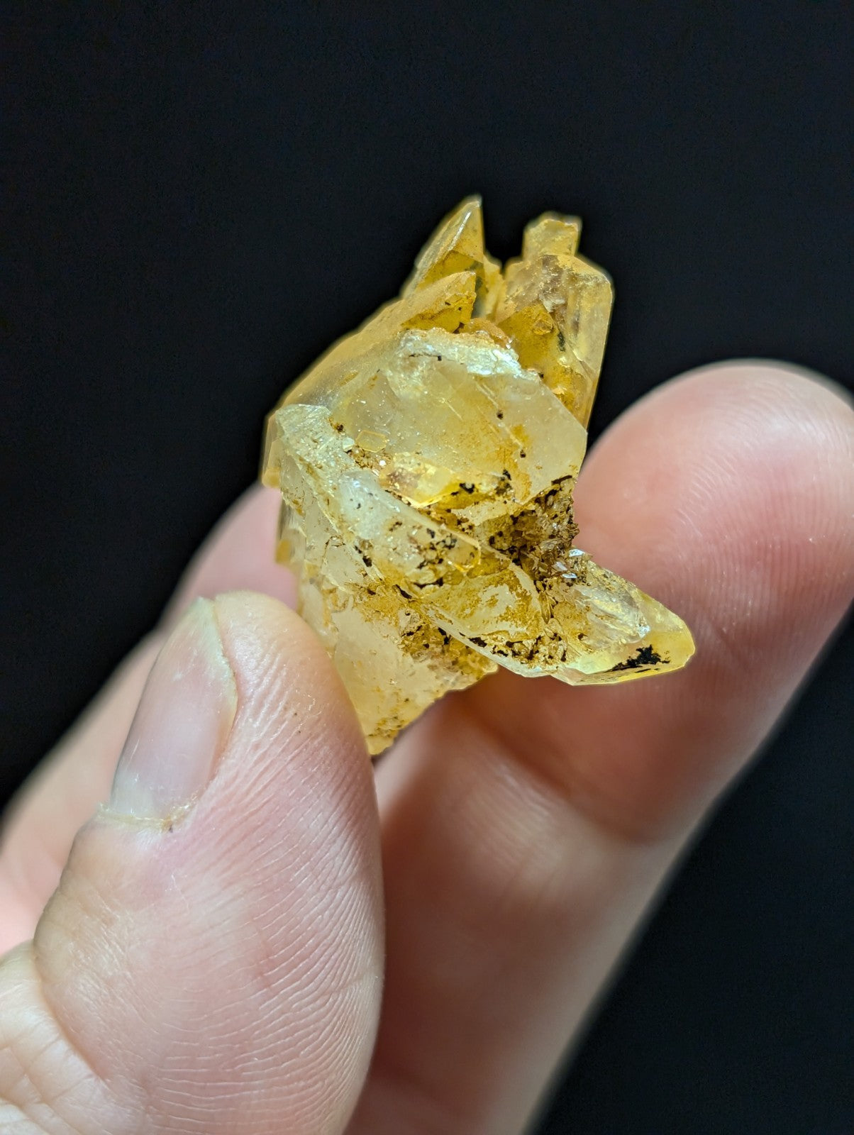 A translucent yellow crystal cluster with jagged, interlocking facets and specks of dark mineral inclusions.