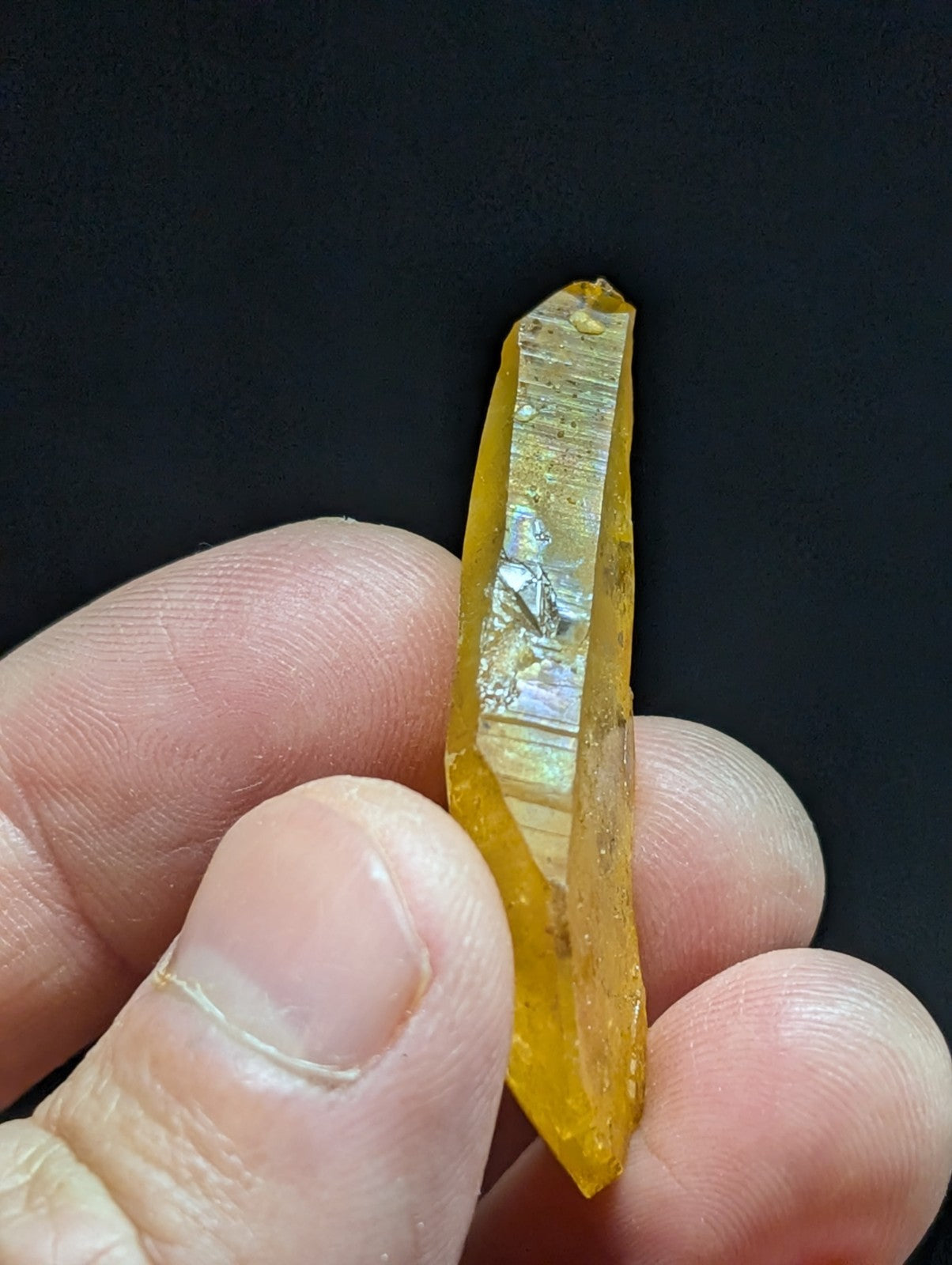 A translucent golden-yellow crystal with a pointed tip and visible internal striations, held gently between fingers.