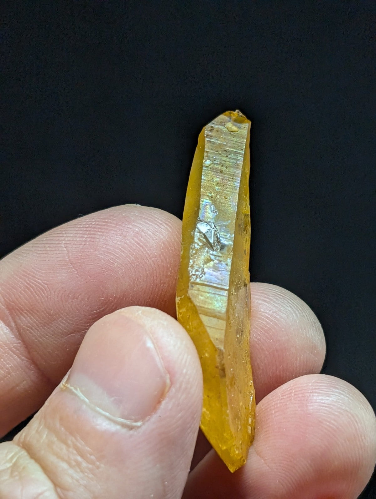 A translucent golden-yellow crystal with a pointed tip and visible internal striations, held gently between fingers.
