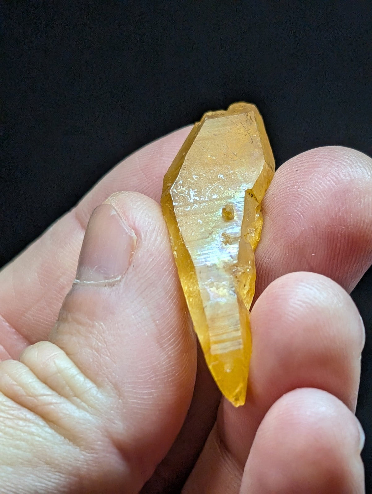 A translucent golden-yellow crystal with a pointed, faceted shape and subtle internal striations.