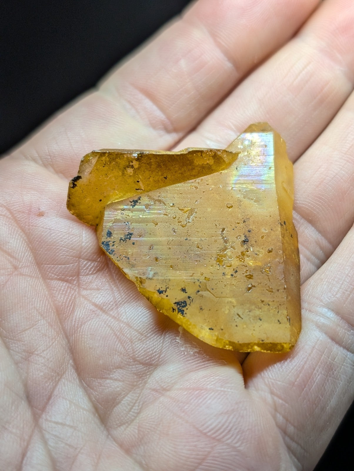 A translucent amber-colored crystal fragment with visible internal striations and dark inclusions, held gently in an open palm.