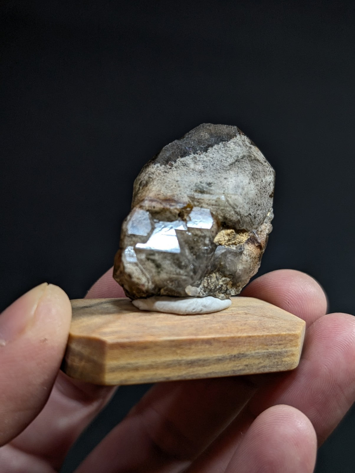 A rough, irregularly shaped mineral specimen with a mix of gray and white hues, featuring prominent reflective crystal facets embedded in its surface.