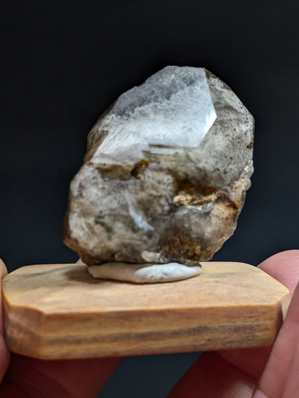 A translucent, grayish quartz crystal with visible internal inclusions and a rough, natural surface rests on a small wooden display stand.
