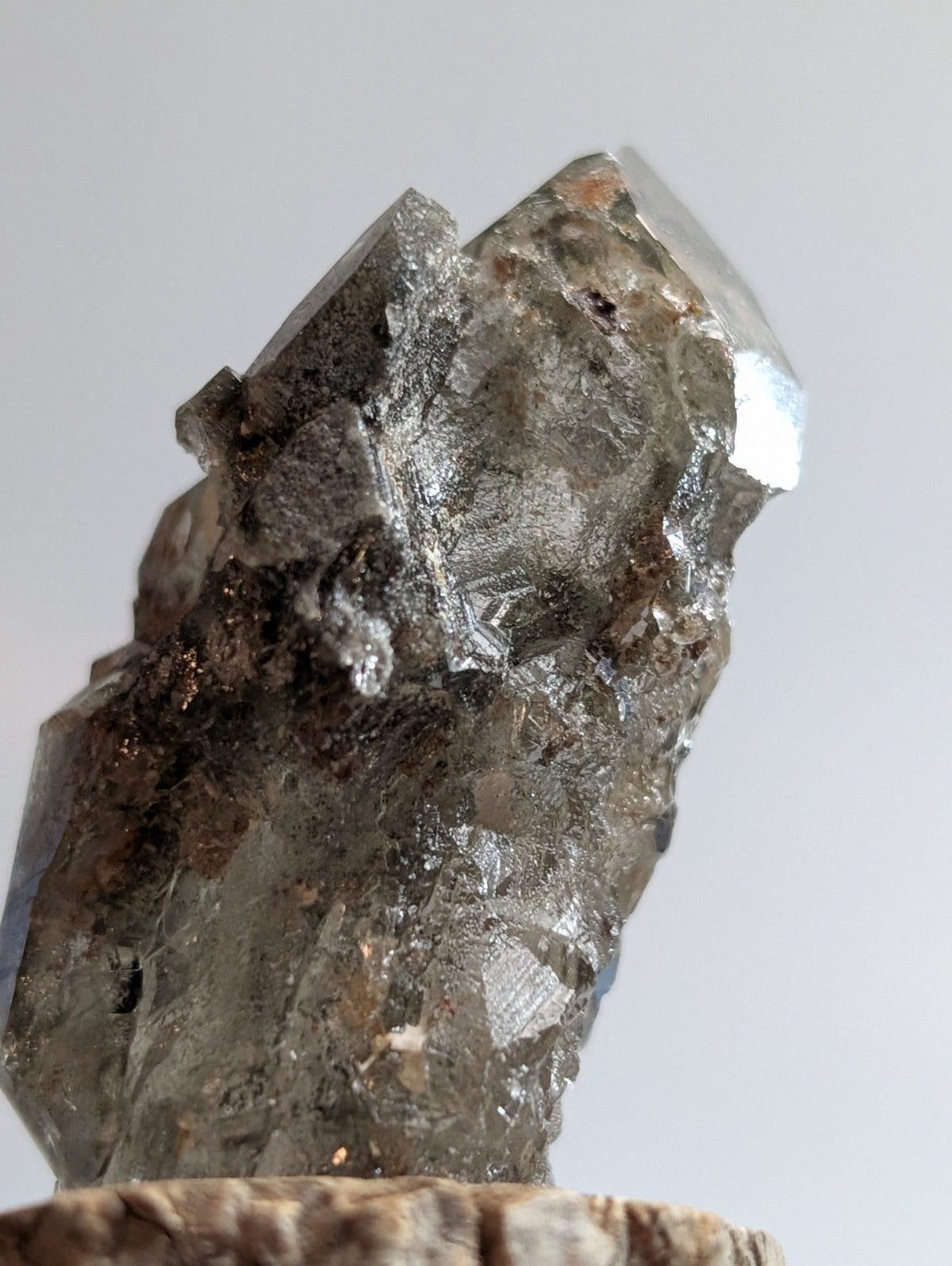 A translucent gray quartz crystal with sharp, angular facets and a rough, earthy base.