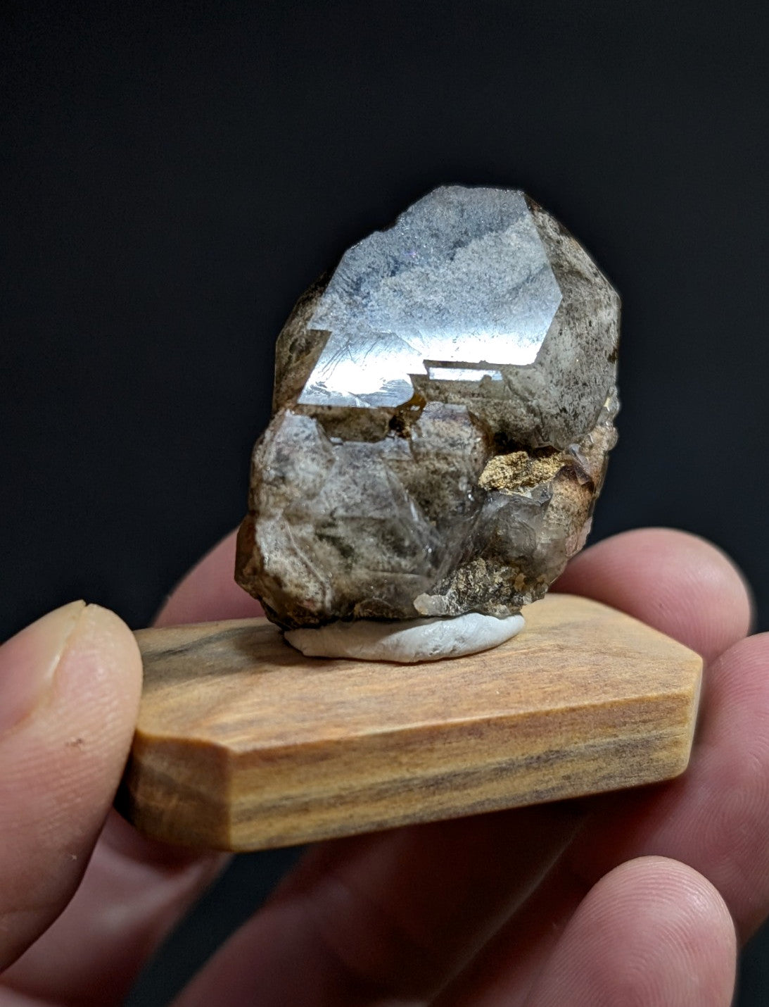 A polished gray mineral specimen with reflective facets, mounted on a wooden display stand.
