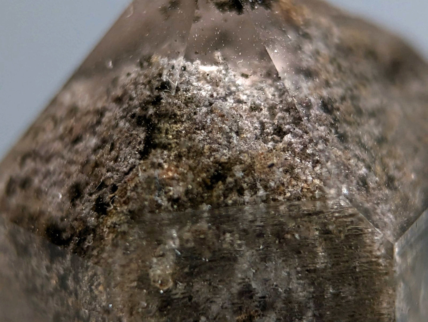 A translucent faceted phantom quartz crystal with dark speckled surface and inclusions on custom wood mount from Arkansas