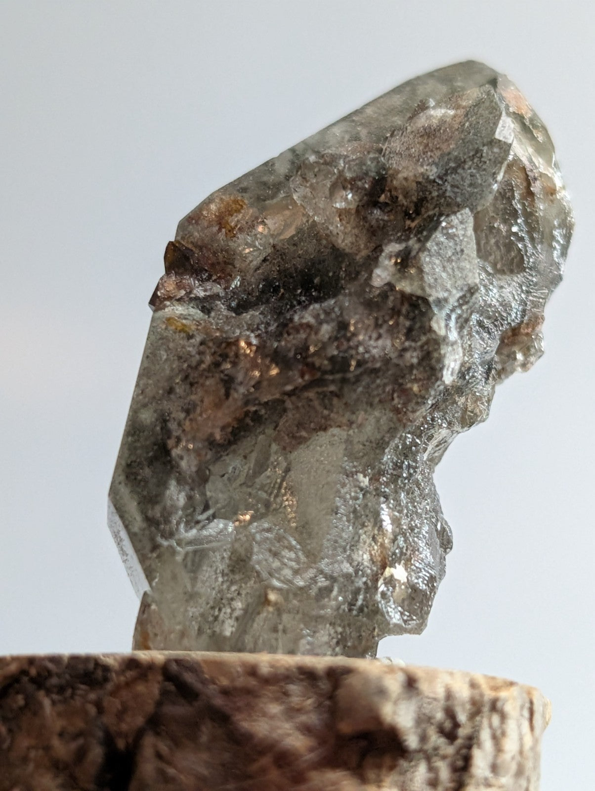 A translucent gray quartz crystal with natural facets and earthy brown inclusions, displayed on a rustic wooden base.