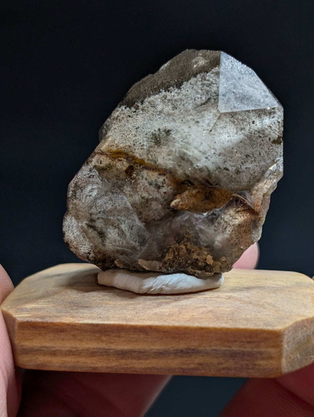 A translucent quartz crystal with a rough, earthy exterior and visible internal facets rests on a wooden display stand.