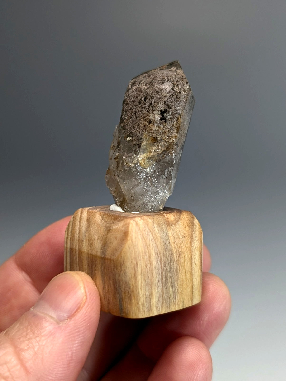 A translucent smoky quartz crystal with a rough speckled surface on a custom light wood mount from Garland County Arkansas