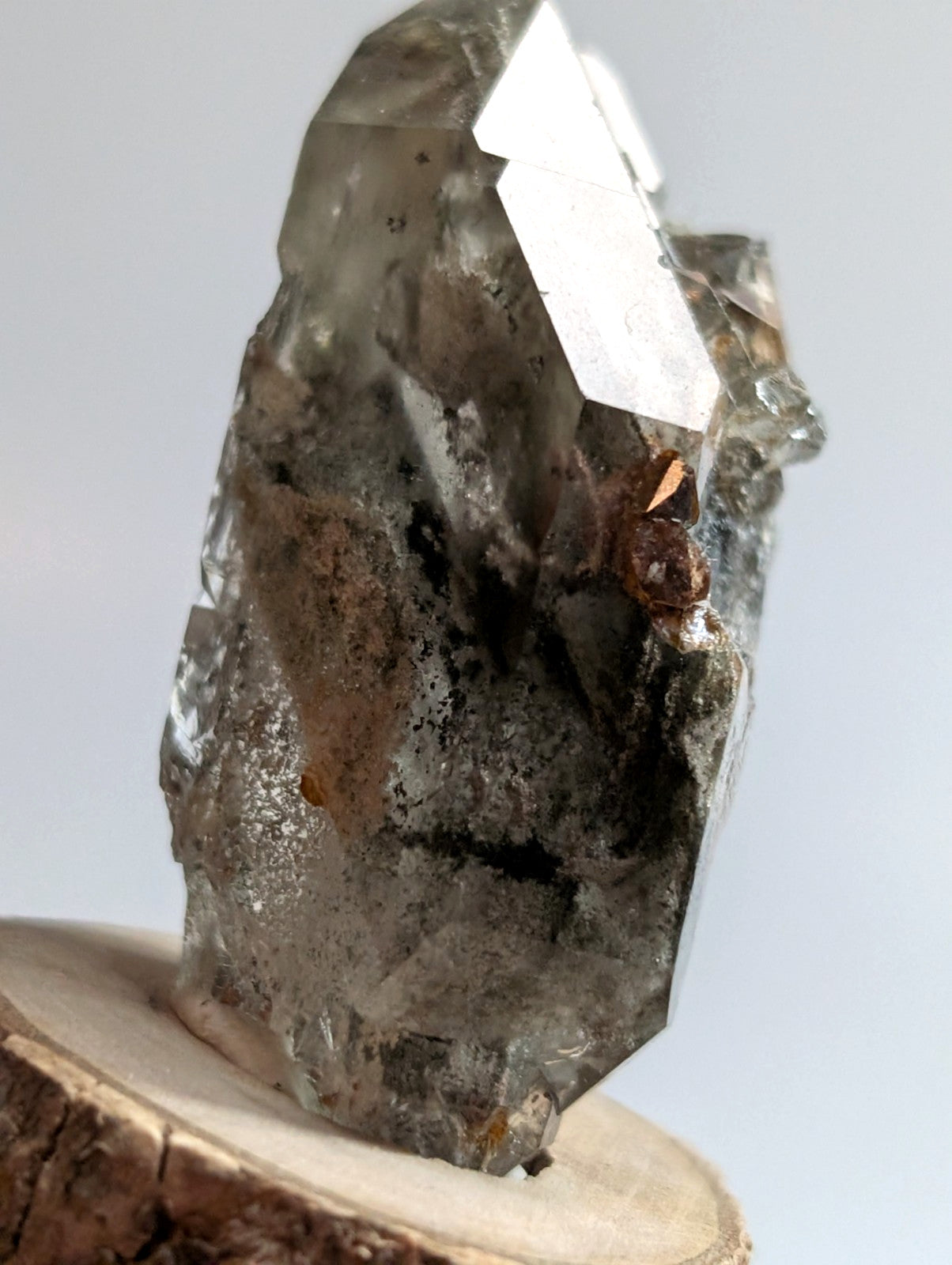 A translucent gray quartz crystal with sharp, angular facets and subtle internal inclusions rests on a circular wooden base.