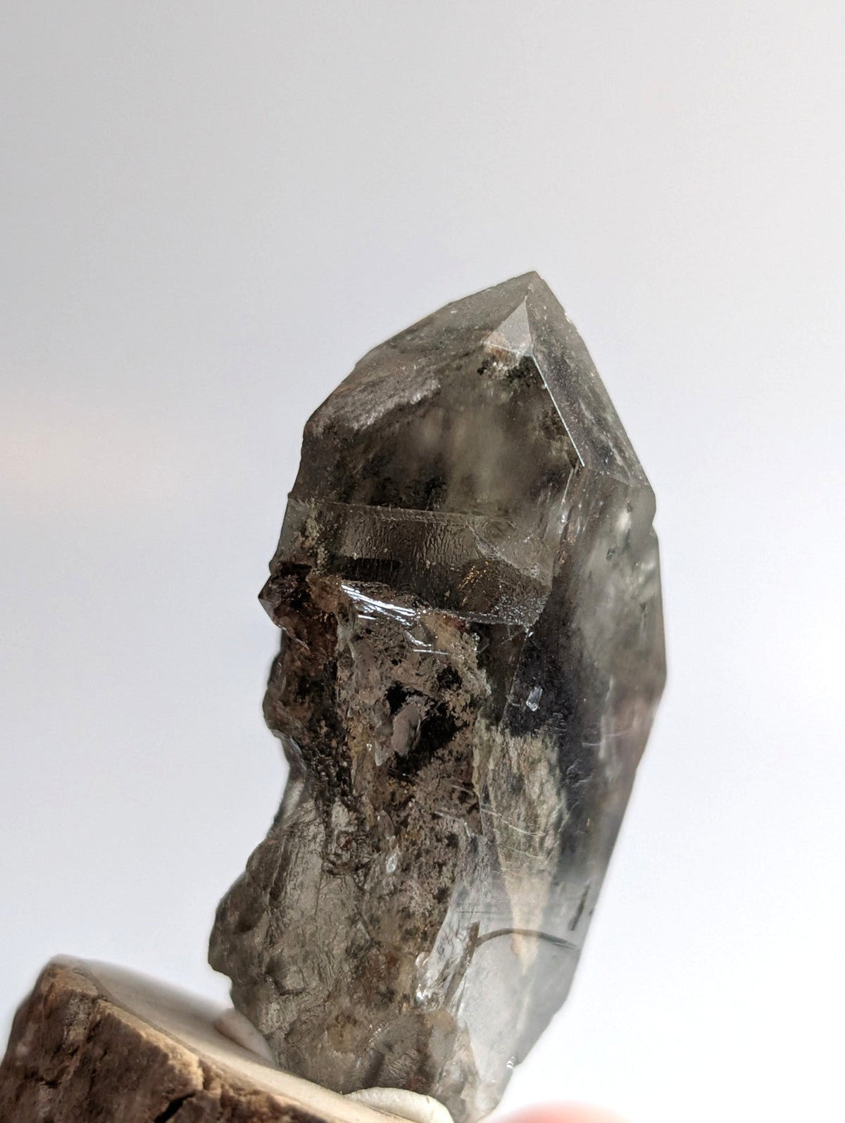 A translucent gray crystal with a pointed, faceted top and rougher base.