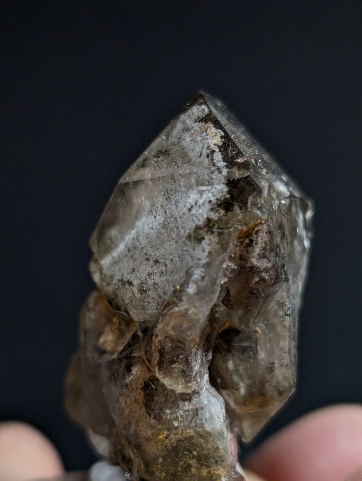 A translucent smoky quartz crystal cluster with a pointed, faceted top and earthy brownish-gray inclusions.