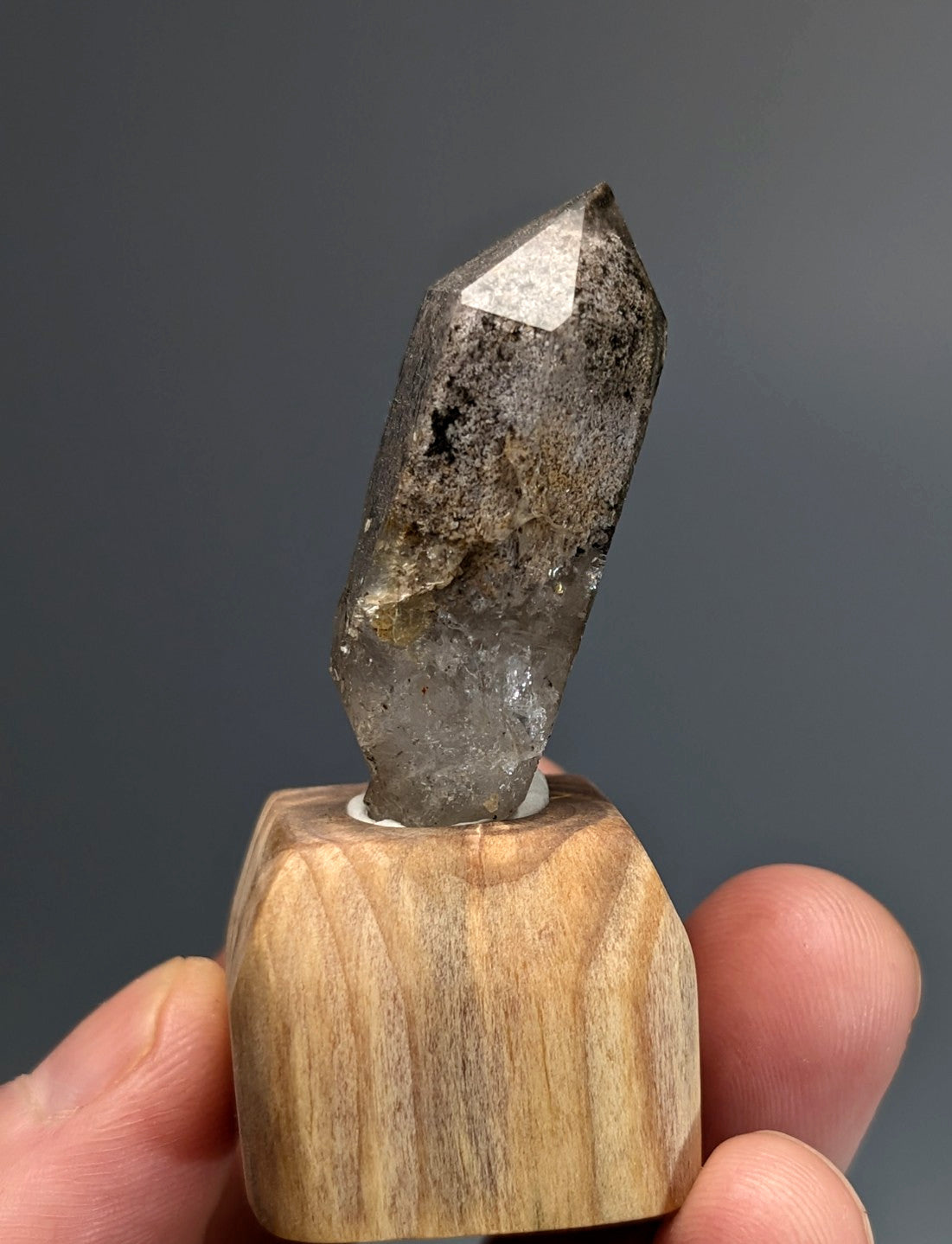 A translucent gray phantom quartz crystal with natural inclusions and pointed tip mounted on custom wood stand from Arkansas