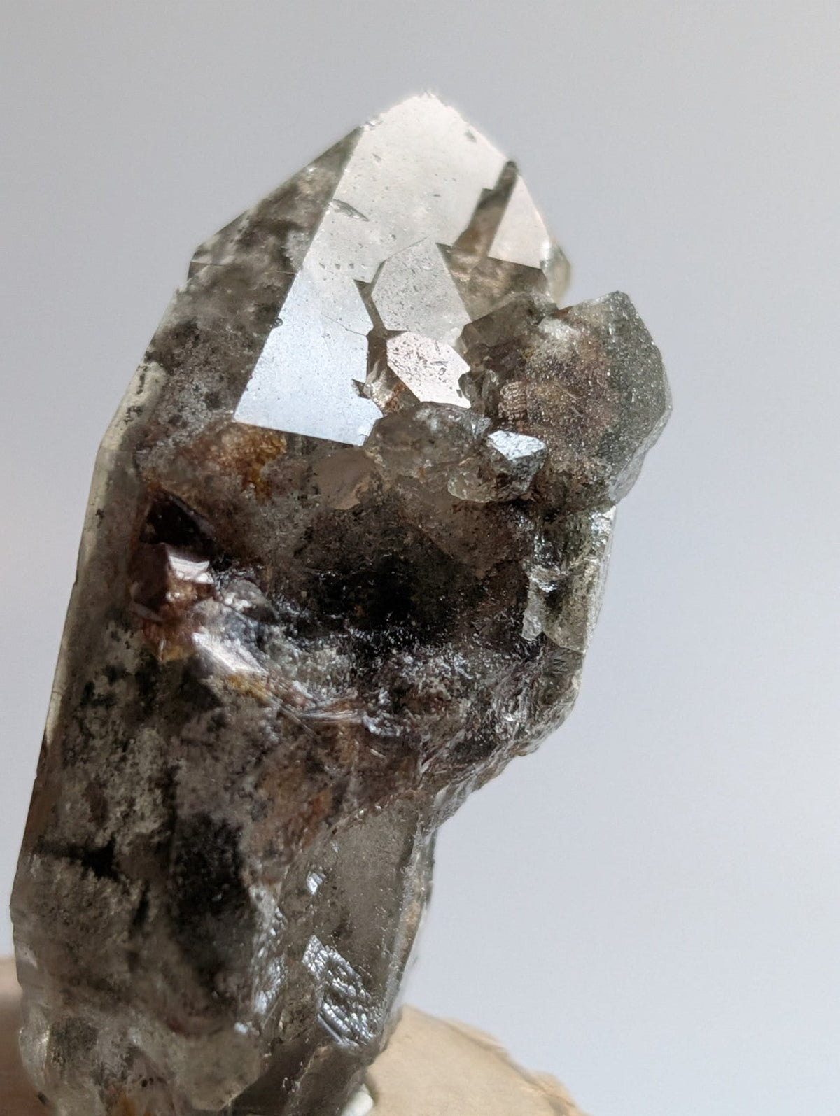 A translucent smoky quartz crystal with a pointed tip and natural inclusions, featuring subtle brownish-gray veining.