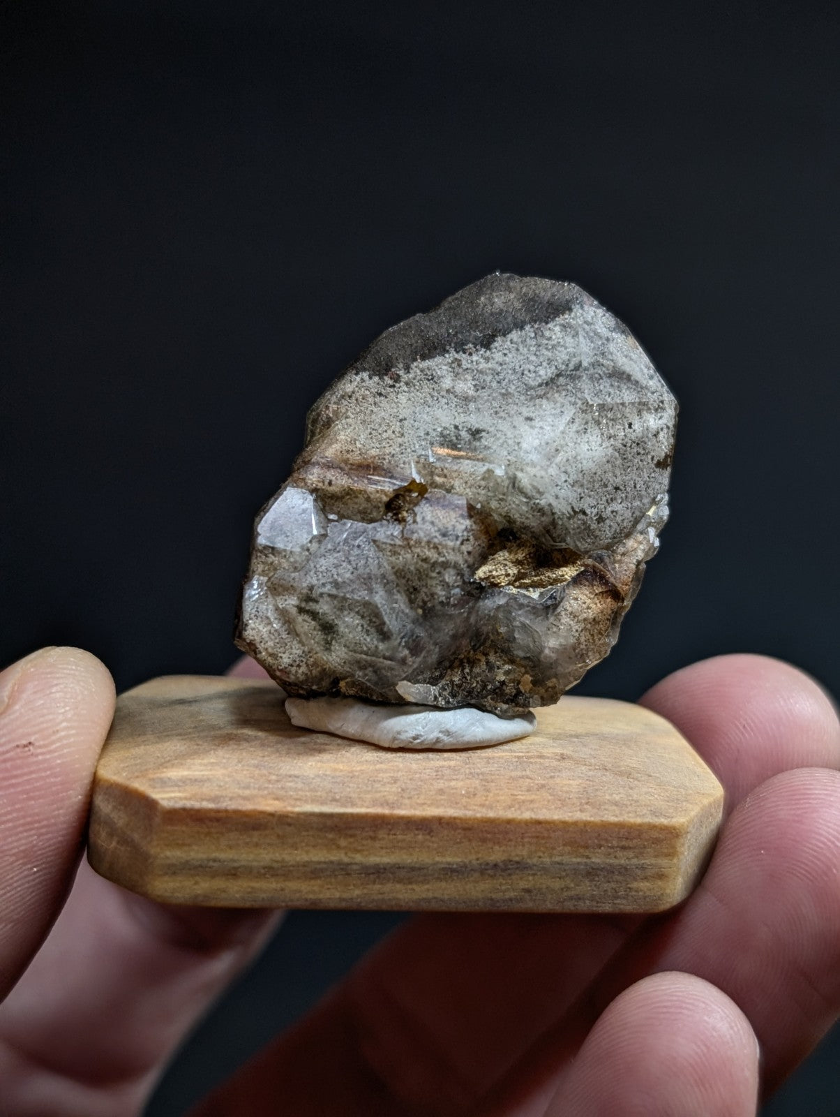 A rough, irregularly shaped mineral specimen with a mix of gray and translucent white crystalline sections resting on a small wooden display stand.
