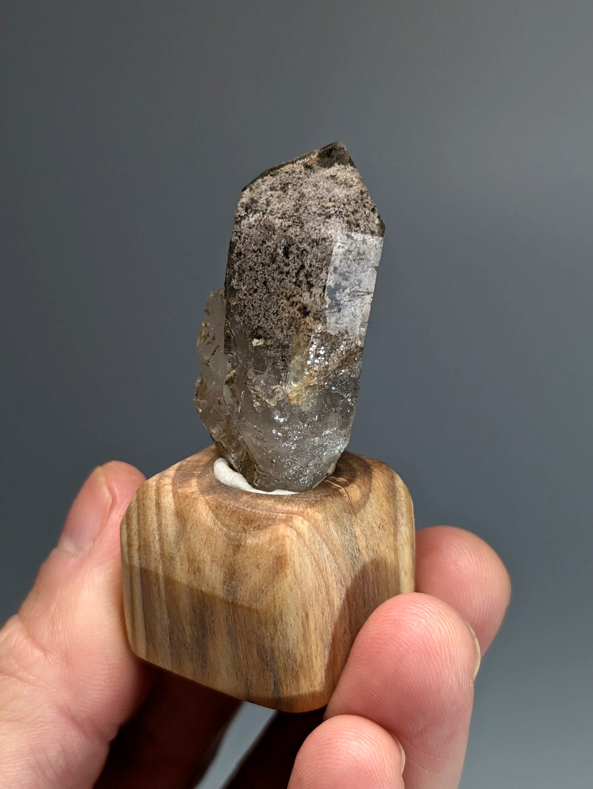 A translucent gray phantom quartz crystal with rough surface and pointed tip on a custom wood mount from Arkansas