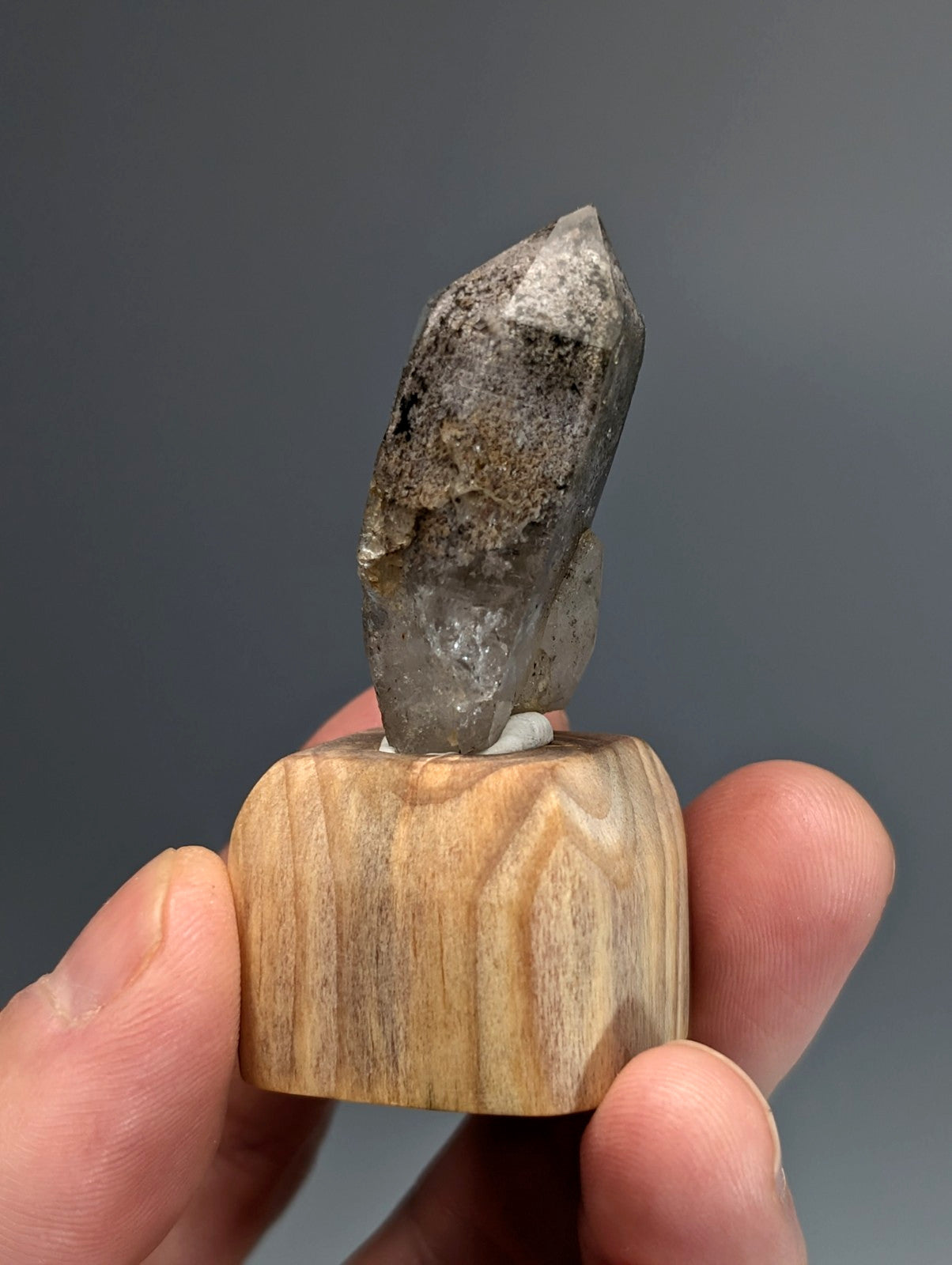 A translucent gray quartz crystal with a pointed tip mounted on a custom light-colored wood base from garland county arkansas