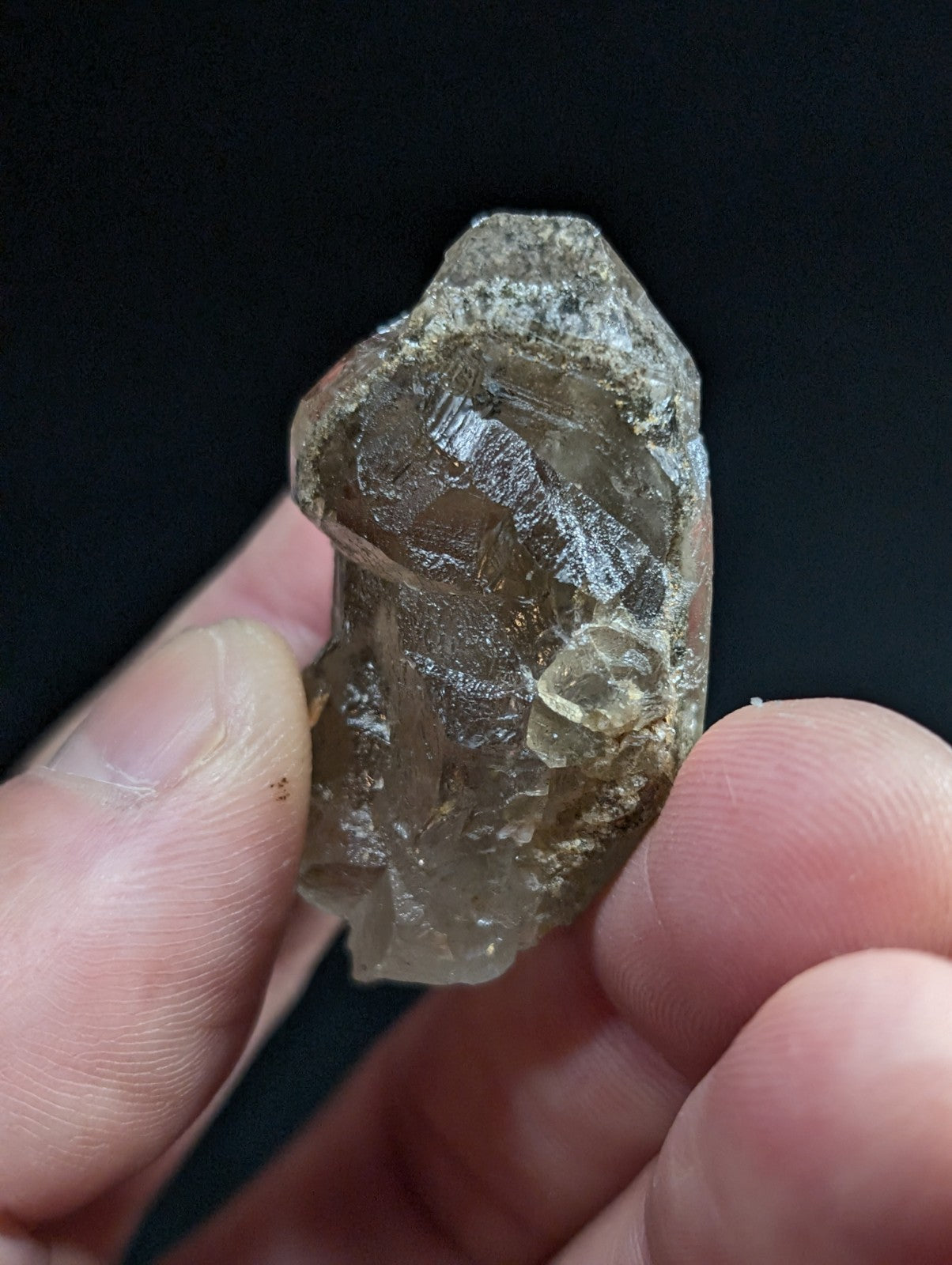 A translucent smoky quartz crystal with natural facets and embedded inclusions, held gently between fingers against a dark background.