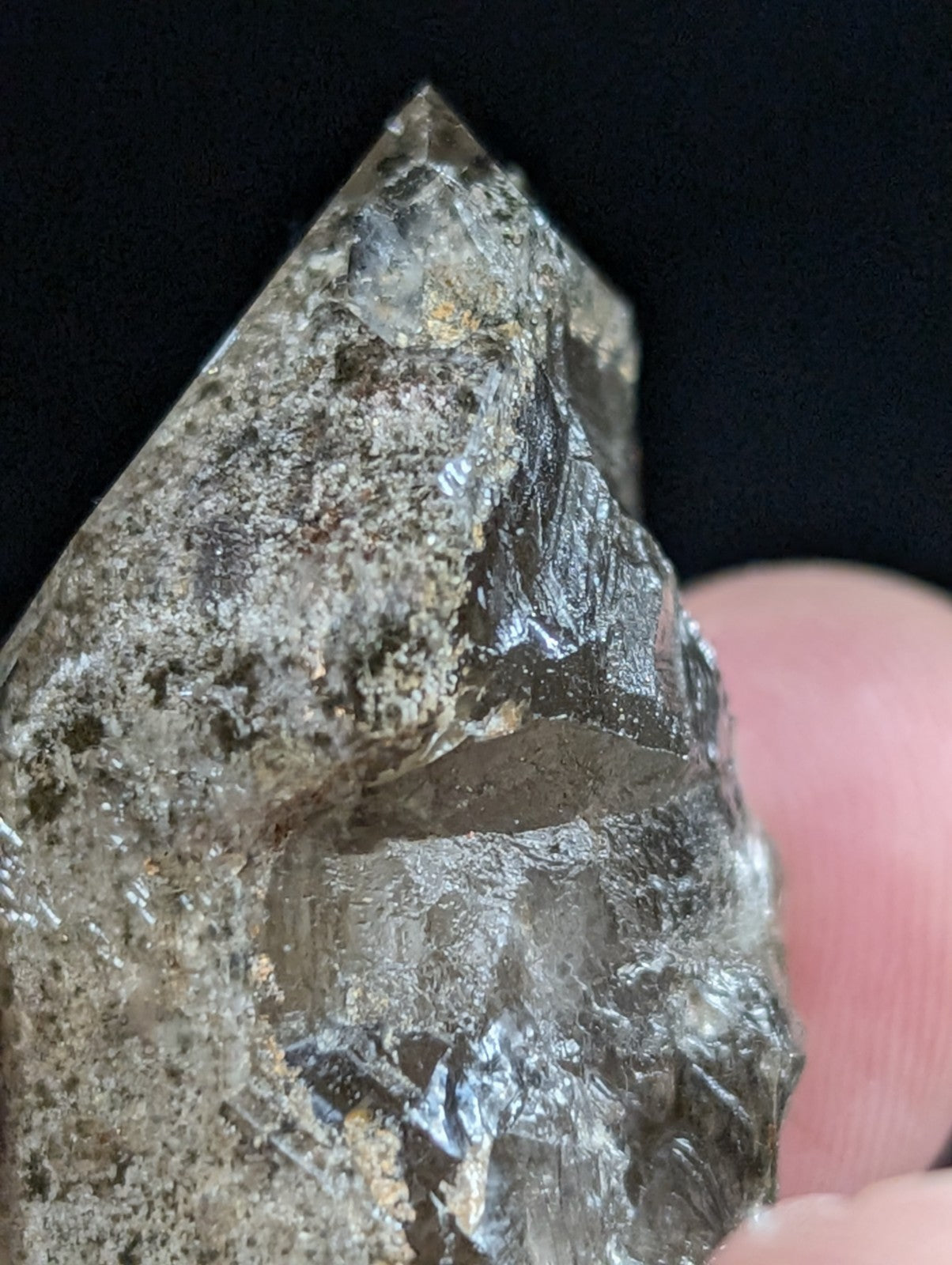 A translucent, smoky quartz crystal with a rough, faceted surface and embedded mineral inclusions.