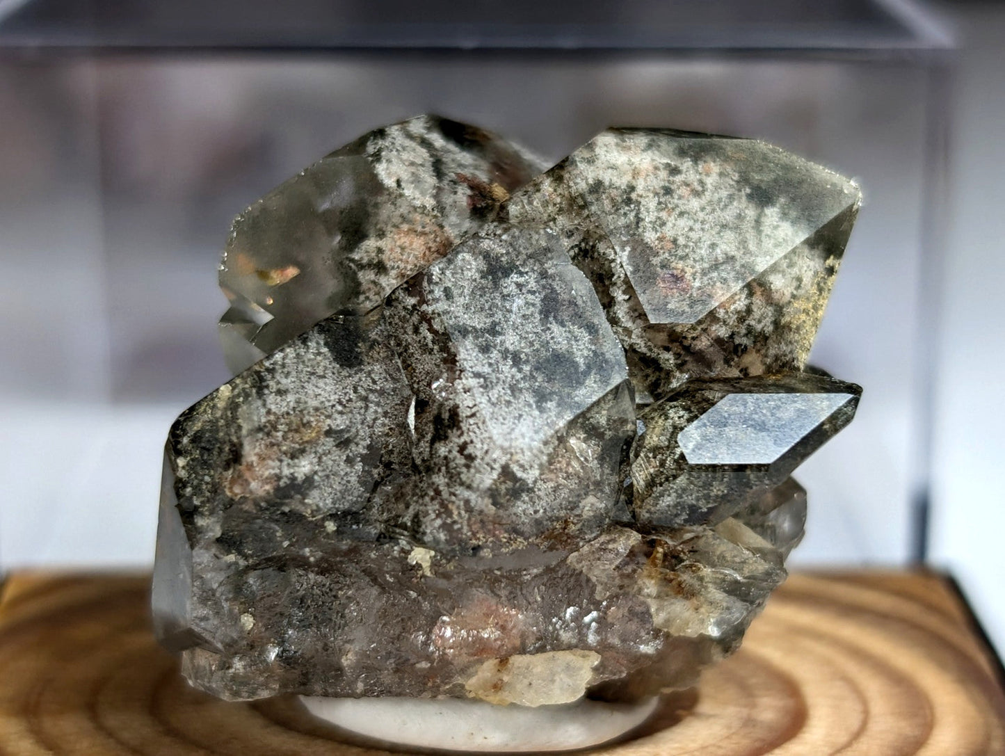 A cluster of translucent, grayish-green quartz crystals with speckled mineral inclusions and sharp geometric facets.