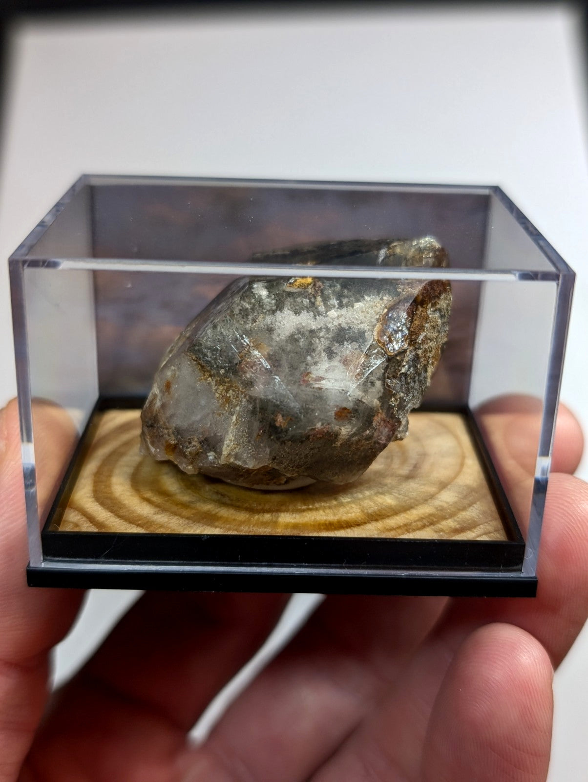 A translucent, irregularly shaped mineral specimen with patches of gray and brown resting inside a clear acrylic display case.