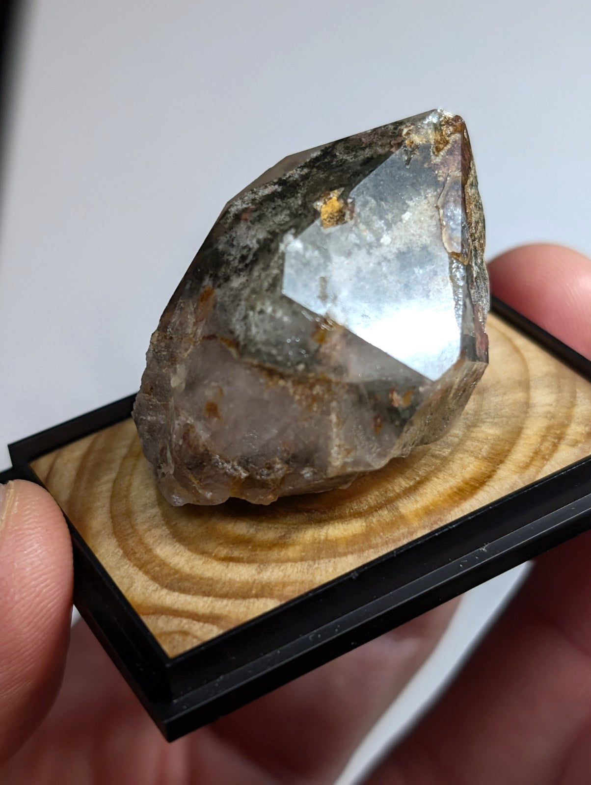 A translucent, faceted quartz crystal with natural inclusions and earthy brownish veining rests on a wooden display base.
